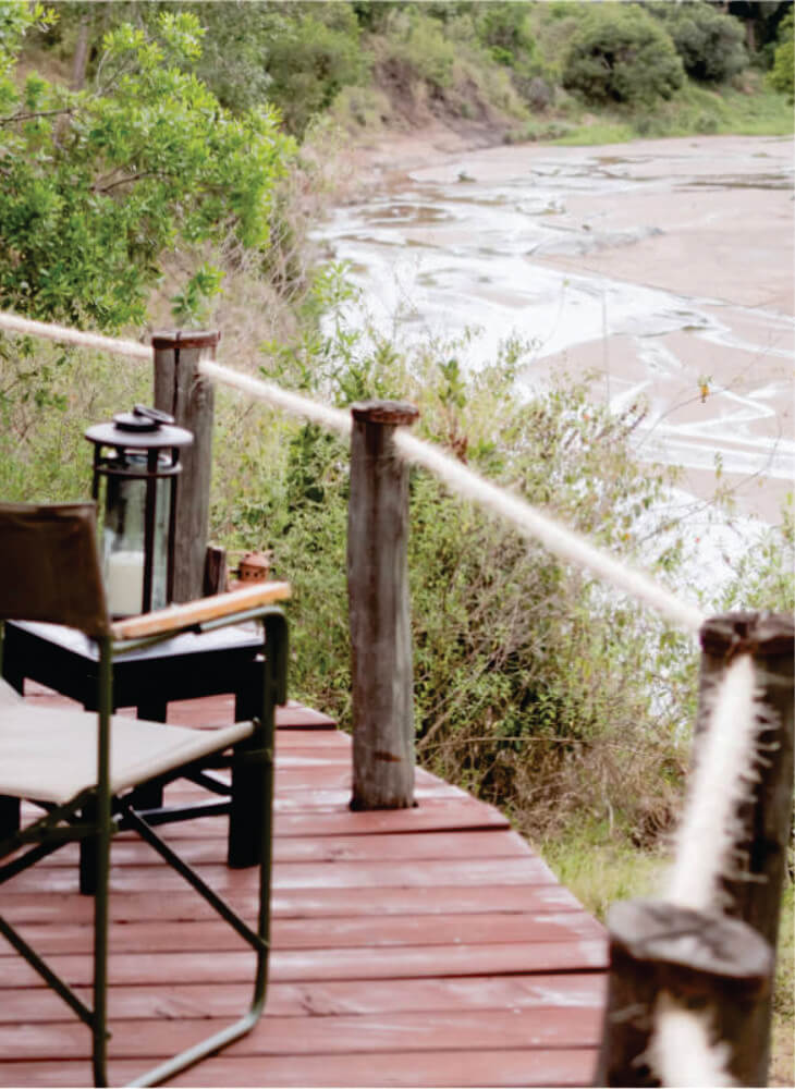 Terrace with a black chair and table facing a river offering a perfect place to spend relaxing moments on budget Masai Mara safari lodge in Masai Mara
