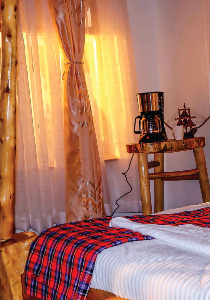 A small wooden table with coffee maker on top near antique bed in a triple room on 2-night budget accommodation in Masai Mara at Lion Sands